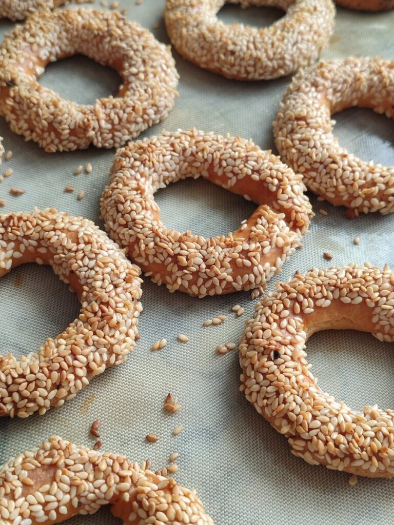 Golden sesame-coated bagels freshly baked and arranged on a baking sheet.